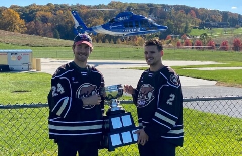 Hershey Bears players holding calder cup in front of a helicopter