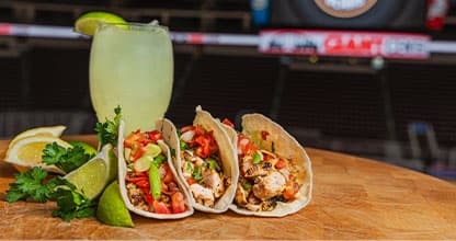 Two brisket tacos on a plate next to a margarita.